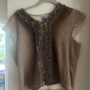 Beige glittrig topp  - Så söt beige melerad, lätt skimrande topp från Here & There,  korta ärmar och volangdetaljer längs halsringningen och framtill! Passar Stl S-M