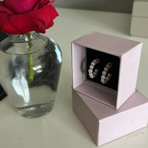 Hoops med pärlor i vit och guld - Snygga örhängen i hoop-modell med vita pärlor runt hela ringen och detaljer i guld. Perfekta för dig som vill ha en klassisk men ändå trendig look. Kommer i en söt ljusrosa ask.