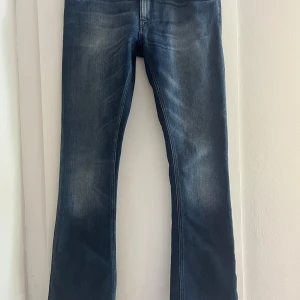 Bootcut jeans från Nudie Jeans blå 31/34 - Snygga blå bootcut jeans från Nudie Jeans i klassisk tvätt med slitningar och markerade sömmar. Jeansen har normal passform och är tillverkade i jeansmaterial. Bakfickorna har Nudie Jeans signatursöm. 