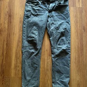 Grå jeansbyxor i regular fit, storlek 30/32 - Snygga grå jeansbyxor från Cubus i storlek 30/32. Modellen är regular fit med klassisk femficksdesign och dragkedja. Jeansen har en mörkgrå tvätt och raka ben, perfekta till sneakers eller boots.
