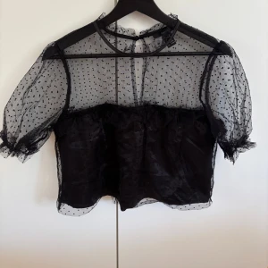 Svart meshblus med prickar Forever 21 - Supersöt svart blus från Forever 21 i mesh med små prickar och volangdetalj över bysten. Blusen har korta puffärmar med resår och ett underlager i silke/satin. Skriv vid frågor💘