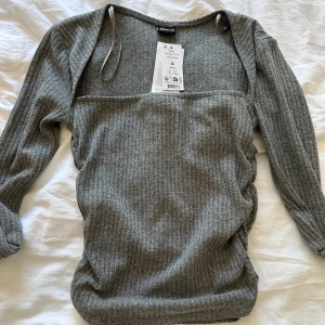 Tajt långärmad  - En grå tajt långärmad tröja ifrån Gina tricot som har lite ”skrynklig” design vid midjan och går lång ut vid urringningen, Som inte säljs längre Helt oanvänd lappen är kvar