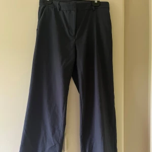 Marinblååa kostymbyxor från Weekday, strl 40 - Blåa kostymbyxor från Weekday i storlek 40. Byxorna har medelhög midja och fickor back och fram. Säljer då jag ej får andvänding av de längre. Är uppsydda så de passar mig 163cm men går att återställa till original längd. Har endast andvänt de ett fåtal gånger.