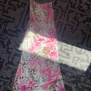 Långklänning med blommor och leopardmönster - Supersnygg långklänning med tunna axelband som knyts. Klänningen har ett unikt mönster med rosa blommor och leopardfläckar på en ljus bas. Perfekt för dig som vill sticka ut med en cool mix av romantiskt och vilt. 