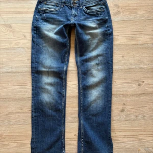 Blå straight jeans från Garcia Jeans - Snygga blå jeans från Garcia Jeans med raka ben och klassisk femficksdesign. Jeansen har dubbla knappar i midjan, slitna detaljer och ljusare partier framtill för en cool, använd look. Modellen heter Rosa och har en straight fit. I slutet är benen klippta på sidan💗