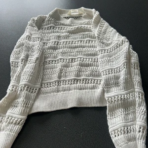 Vit stickad tröja från H&M - Superfin vit stickad tröja från H&M med snyggt hålmönster och ribbade muddar. Tröjan har lång ärm och är lite croppad i modellen, perfekt till jeans eller kjol. Mjuk och skön, passar både till skolan och häng med kompisar.
