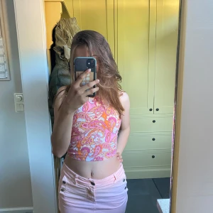 Färgglad halterneck linnetopp paisley - Säljer en croppad halterneck topp med paisleymönster i rosa, orange och vitt. Toppen har smala knytband i nacken och är ärmlös, perfekt för varma dagar. Materialet känns lätt och svalt, och toppen har en riktigt somrig vibe.