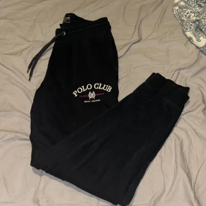 Svarta mjukisbyxor Polo Club M - Svarta mjukisbyxor från Polo Club med logga och text på vänster lår. Byxorna har dragsko i midjan, resår vid benslut och en bakficka. Perfekta för chill eller träning, riktigt sköna och stilrena.