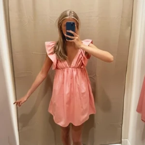 Volang klänning - Supersöt rosa kortklänning med djup v-ringning och volangärmar. Klänningen har en luftig passform och är perfekt för varma dagar. 