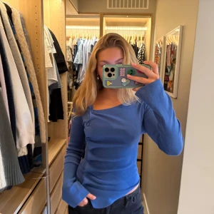 Blå asymmetrisk topp från Zara - Säljer en blå långärmad topp från Zara med asymmetrisk knäppning och snygg v-ringad hals. Modellen är figurnära.