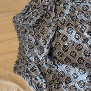 Blåmönstrad kortklänning Gina Tricot - Supersöt blå och vit kortklänning från Gina Tricot med smockad överdel och blommigt mönster. Klänningen har ärmlös design och är perfekt för varma dagar. Lätt och luftig känsla, passar dig som gillar en chill och trendig stil.