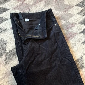 Svarta manchesterbyxor med raka ben - Säljer ett par svarta manchesterbyxor med klassisk femficksmodell och raka ben. Byxorna har dragkedja och knapp framtill, samt mjuk och skön manchesterstruktur. Perfekta för dig som gillar en stilren och tidlös look.