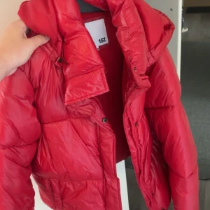 Röd pufferjacka från 157 - Säljer en riktigt fet röd pufferjacka från 157. Jackan har hög krage, dragkedja och tryckknappar framtill. Den är vadderad och har en schysst oversized look som håller dig varm under kalla dagar. Perfekt för dig som vill sticka ut med färg i vinter.