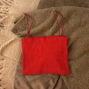 Röd ribbad linne-topp från Zara - Säljer en röd ribbad linne-topp från Zara med tunna axelband. Toppen är croppad och har en enkel, stilren design som passar perfekt till jeans eller kjol. Materialet är mjukt och stretchigt för en bekväm passform.