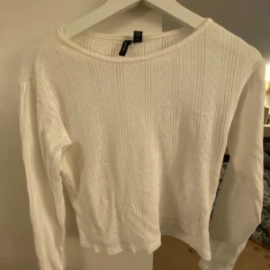 Vit ribbad långärmad tröja Vero Moda - Supersöt vit långärmad tröja från Vero Moda i ribbad bomull med diskret hålmönster. Tröjan har en rund halsringning och sitter snyggt med normal passform. Perfekt till jeans eller kjol för en fräsch look.