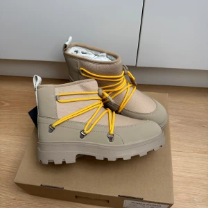 Tretorn Alnarp Hybrid 39 - Snygga beige Tretorn Alnarp Hybrid boots med chunky sula och gula snören. Skorna har robust design, grovt mönstrad yttersula och detaljer i syntet och textil. Perfekta för dig som gillar outdoor-vibe och vill sticka ut med färgglada snören.