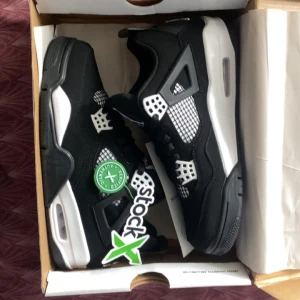 Nike Air Jordan 4 svart/vit sneakers - Säljer ett par Nike Air Jordan 4 sneakers i svart och vitt med klassisk meshpanel och coola plastdetaljer. Skorna har en chunky sula med synlig Air-enhet och ikoniska vingar vid snörningen. Perfekta för dig som vill sticka ut med en tidlös streetwear-look.