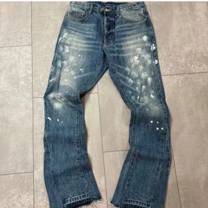 Blå jeans med slitna detaljer - Säljer ett par blå jeans med coola slitna detaljer och fransar vid bensluten. De har en klassisk femficksdesign och en knappgylf. Perfekta för en avslappnad stil.