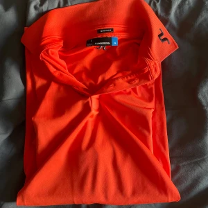 Orange pikétröja från J.Lindeberg - Säljer en snygg orange pikétröja från J.Lindeberg. Tröjan har en klassisk krage och korta ärmar med märkets logga på ärmen. Perfekt för en sportig look eller en avslappnad dag ute. Jätte snygg golf piké som inte har några hål eller fläckar 