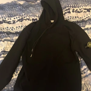 Svart hoodie från Stone Island - Säljer en stilren svart hoodie från Stone Island med deras ikoniska märke på ärmen. Perfekt för en casual look med en skön passform och huva. Hör av dig vid intresse!