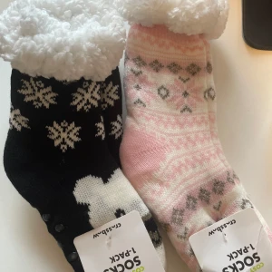 Mysiga strumpor med snöflingor och mönster - Två par mysiga strumpor med fluffigt foder. Ett par är svart med vita snöflingor och det andra är rosa med grått mönster. Perfekta för kalla dagar. ett par kostar 55 kr.