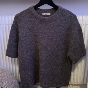 Grå/brun stickad tröja från Gina Tricot - Säljer en mysig grå stickad tröja från Gina Tricot i premiumkvalitet. Tröjan har korta ärmar och en rund halsringning. En stilren och bekväm baströja för garderoben.