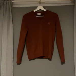 Orange v-ringad tröja - Säljer en snygg orange v-ringad tröja från Newhouse. Tröjan har långa ärmar och en diskret broderad blomma på bröstet. Perfekt för en stilren look. Storlek står inte men skulle säga S-M.