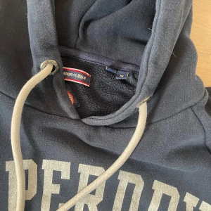 Superdry hoodie - Säljer denna extremt snygga Superdry hoodie med ett sjukt fett tryck. Hoodien är i nyskick, knappt använd och i storlek M. Hör av er vid eventuella frågor eller funderingar! 