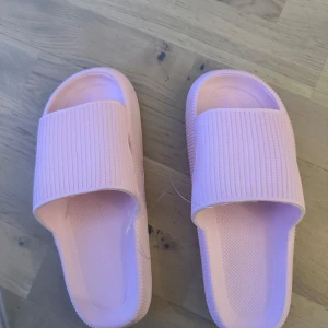Rosa sandaler med ribbad yta flops tofflor - Säljer ett par rosa sandaler med ribbad yta och bekväm sula. Perfekta för sommarens varma dagar. De har en enkel och stilren design som passar till det mesta. Ett par standard tofflor till oslagbart pris! Dessa cloud tofflor kommer i en ny modern tappning med stötdämpande sula och som passar till flera olika tillfällen, om du så ska ner till stan eller bära dem hemma. De gör dina steg fjäderlätta. Börja gå på moln igen med dessa flops!