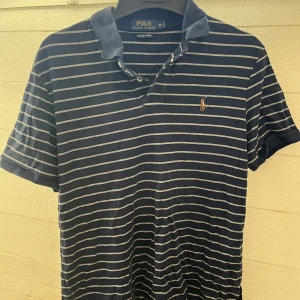 Blå randig pikétröja från Ralph Lauren - Säljer en klassisk blå pikétröja från Ralph Lauren med vita ränder och broderad logga