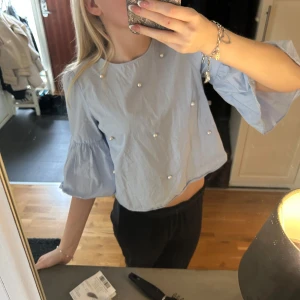 Ljusblå blus med pärldetaljer - Säljer en söt ljusblå blus med pärldetaljer. Blusen har trekvartsärmar med volang och en lös passform. Skriv för frågor 💛
