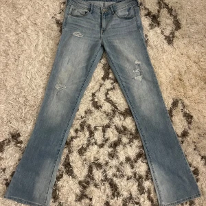 Blå lågmidjade bootcut jeans - Snygga blå bootcut jeans med slitna detaljer på framsidan. De har en klassisk femficksdesign och en ljus tvätt som ger en avslappnad look. Perfekta för en trendig stil. W28 L33. Passar som storlek 34/36