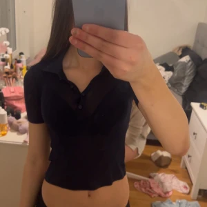 Svart kortärmad polotopp - Snygg svart kortärmad polotopp med knappar framtill. Perfekt för en stilren look. Toppen är figurnära och har en klassisk krage.