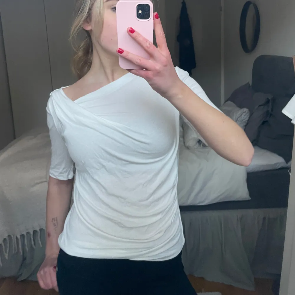 Säljer en stilren vit omlottopp med trekvartsärm. Toppen har en elegant drapering och en asymmetrisk halslinje som ger en unik look. Perfekt för både vardag och speciella tillfällen. Endast testad!. Yläosat.