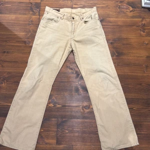Beige byxor från Marlboro Classics - Snygga beige byxor från Marlboro Classics med klassisk design. Byxorna har en rak passform och är tillverkade i ett slitstarkt material. Perfekta för en avslappnad stil. Nypris cirka 1200 kronor