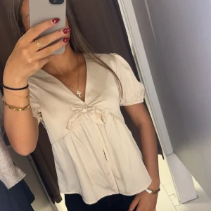Beige blus med rosett - Säljer en söt beige blus med korta ärmar och en fin rosett framtill. Helt ny aldrig använd 
