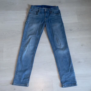 Blå jeans från Levi's - Snygga blå jeans från Levi's med en klassisk femficksdesign och knappgylf. De har en straight passform och är perfekta för en avslappnad stil. Levi's-loggan syns på insidan av midjan. Levis 512