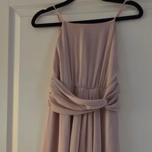 Ljusrosa klänning från Lipsy - Elegant ljus gammelrosa klänning från Lipsy med smala axelband och en vacker drapering i midjan. Klänningen har en dragkedja i ryggen för enkel påklädning. Perfekt för sommarens festligheter. Använd 2 ggr ny pris 550:-