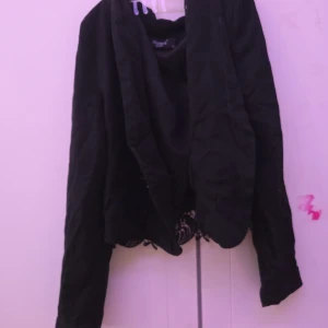 Svart jacka med spetsdetaljer - Snygg svart jacka med långa ärmar och vackra spetsdetaljer längs nederkanten. Perfekt för att ge en elegant touch till din outfit.