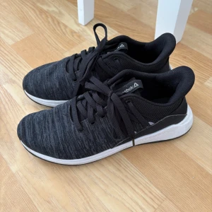 Svarta sneakers från Reebok - Snygga och bekväma svarta sneakers från Reebok med en stilren design. Skorna har snörning och en vit sula som ger en modern touch. Perfekta för både träning och vardag.