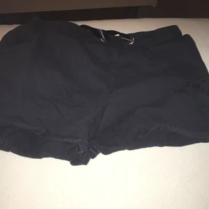 Mörkblåa shorts med broderad detalj - Snygga mörkblåa shorts med en broderad detalj på sidan. De har en elastisk midja med snörning för justerbar passform. Perfekta för en avslappnad stil.