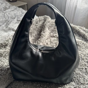 Handväska  - Snygg svart väska med en praktisk dragkedja upptill och en rundad form som ger den ett modernt utseende. Perfekt för att bära dina dagliga nödvändigheter. Väskan är knappt använd så så gott som ny. Nypris 499kr💞