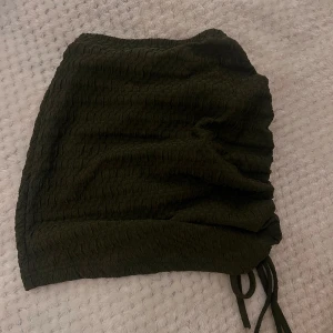 Militärgrön kjol med snörning -  kortkjol med snörning på sidan. Kjolen har en texturerad yta. Perfekt för att styla med olika toppar! Aldrig använt! 