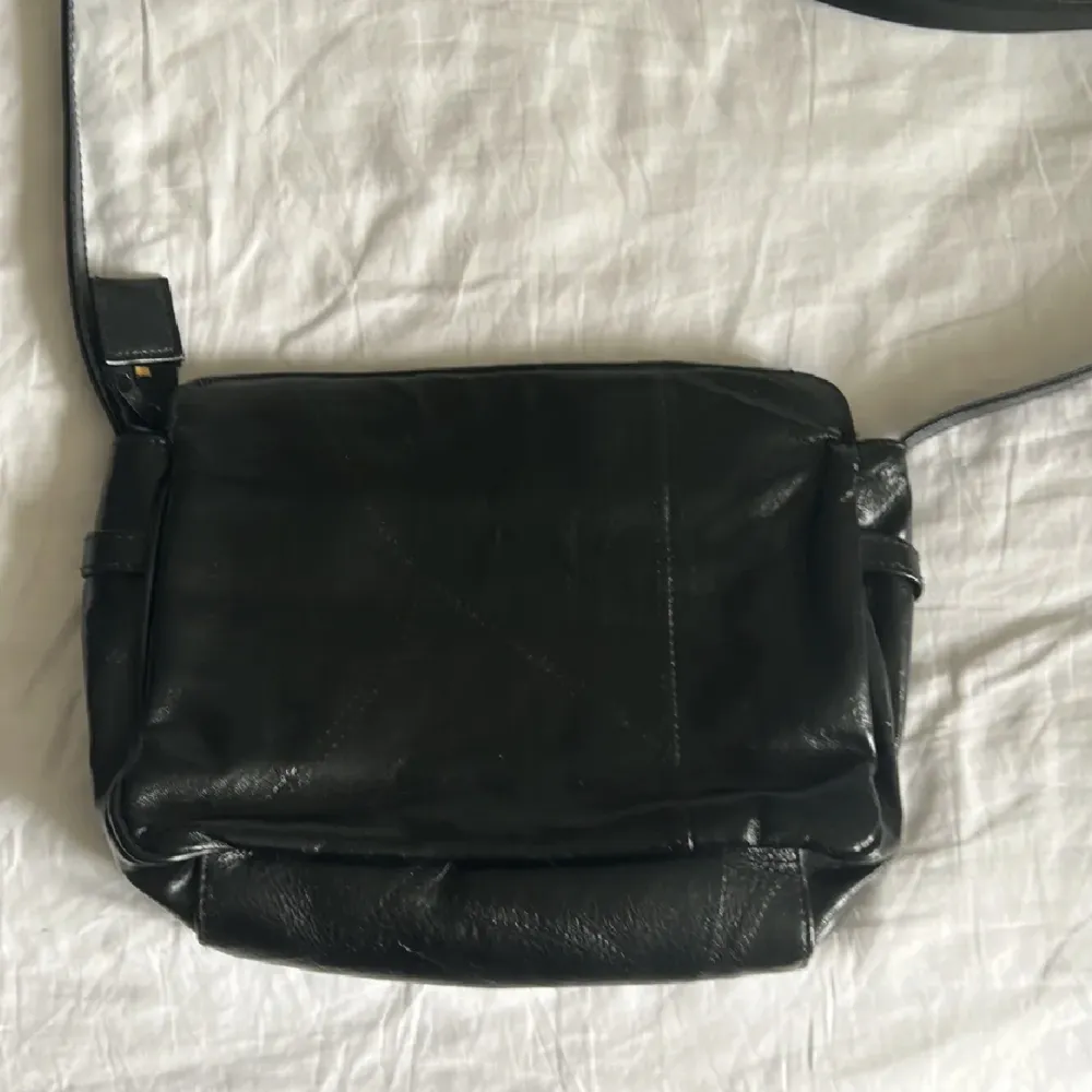 En gullig axelremsväska i svart fuskläder. Knappt använd och i typ nyskick. Ungefär 30 cm bredd och 20 cm höjd. . Laukut & Käsilaukut.