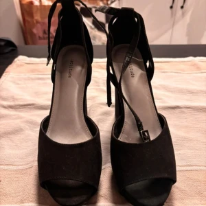 Svarta klackskor från Attitude - Snygga svarta klackskor från Attitude med öppen tå och justerbara remmar runt ankeln. Skorna har en hög klack och är perfekta för en kväll ute. Bra skick, finns småtecken på slitage Storlek 37 Använd några gånger.