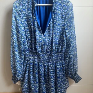 Blå mönstrad klänning från Zara! - Säljer en blå mönstrad klänning från Zara med långa ärmar och v-ringad design. Säljer då den inte kommer till användning, använd max 2 gånger. Hör av er vid frågor eller mer bilder!🩷(köparen står för frakten)