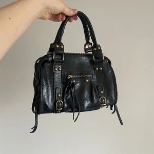 Svart handväska med nitar - Snygg svart handväska i ”skinn” med coola nitar och dragkedjedetaljer i guld. Typ helt oanvänd! Köpt i Italien 