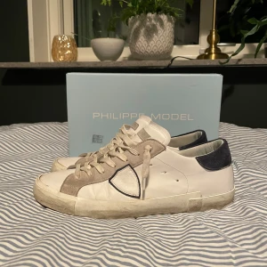 Philippe Model - Snygga vita sneakers från Philippe Model med gråa och mörkblå detaljer. Skorna har en klassisk design med snörning och en bekväm passform. Perfekta för en stilren look. Mycket bra skick 9/10, sparsamt använda. Köpta på cetire för nån månad sen. Kvitto finns. Kom privat för funderingar 😁