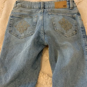 Ljusblå low waist bootcut jeans med broderade fickor - Snygga ljusblå jeans med broderade detaljer på bakfickorna. De har en klassisk femficksdesign och bälteshällor. Perfekta för en avslappnad stil med en touch av elegans.