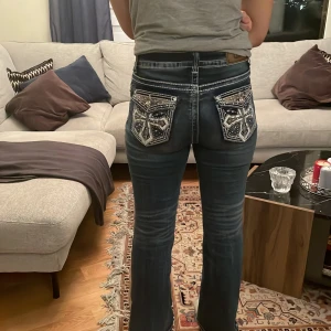 Sänkt pris! Jeans med broderade bakfickor - Snygga jeans med unika broderade bakfickor i ett korsmönster. Jeansen har en mörkblå tvätt och en bootcut-stil som ger en klassisk look. Perfekta för dig som vill ha något extra i garderoben. Har endast endast fåtal gånger.  Som heltänt. Köpts i USA märket är T& Y fashion storlek  9/10 (small och passar en som ör ca 165-170 cm lång)